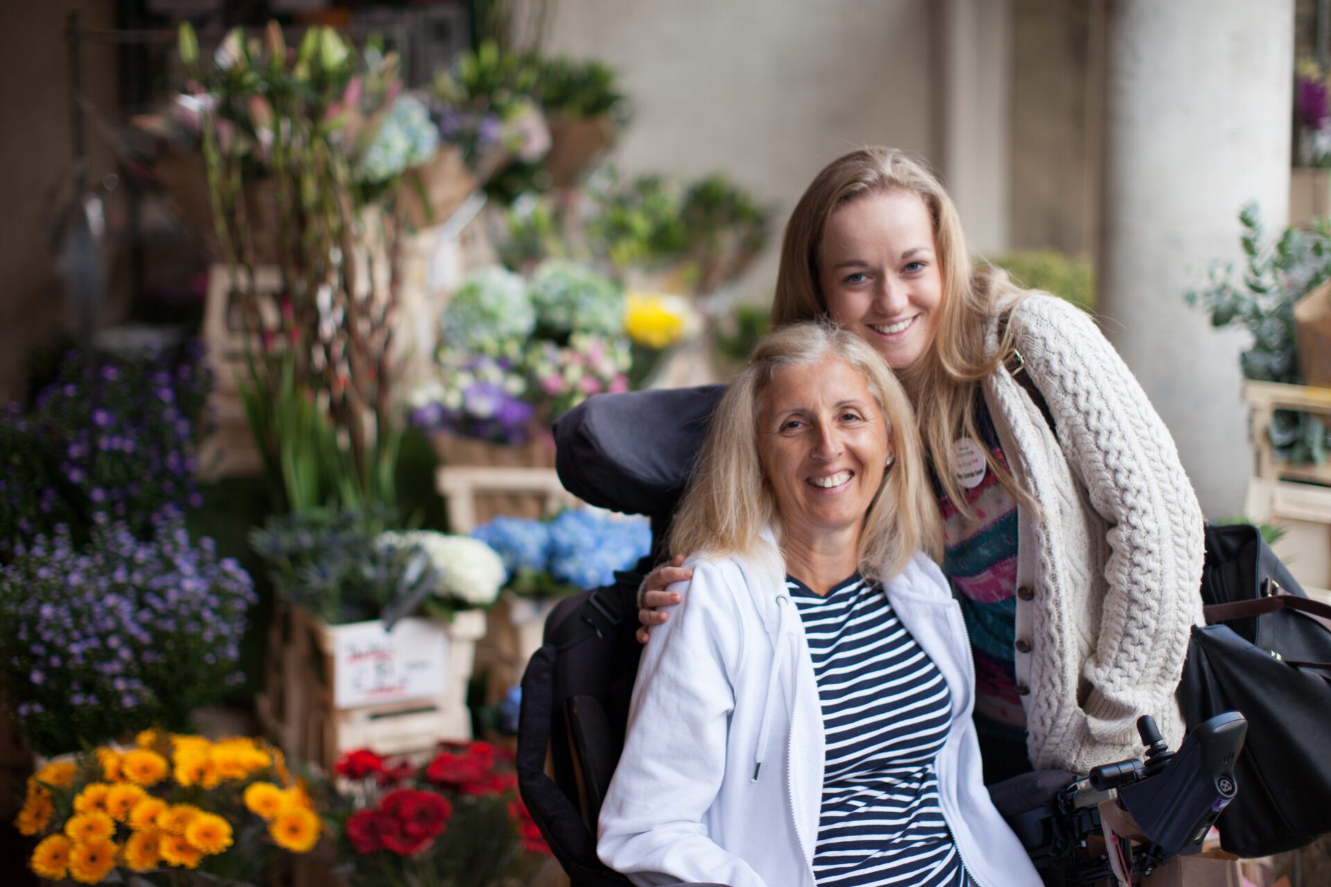 Woman in a wheelchair smiling with another young woman next to her while on a shopping excursion during a Revitalise break