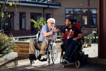 Two men in wheelchairs holding hands in Revitalise Jubilee Lodge's outdoor courtyard