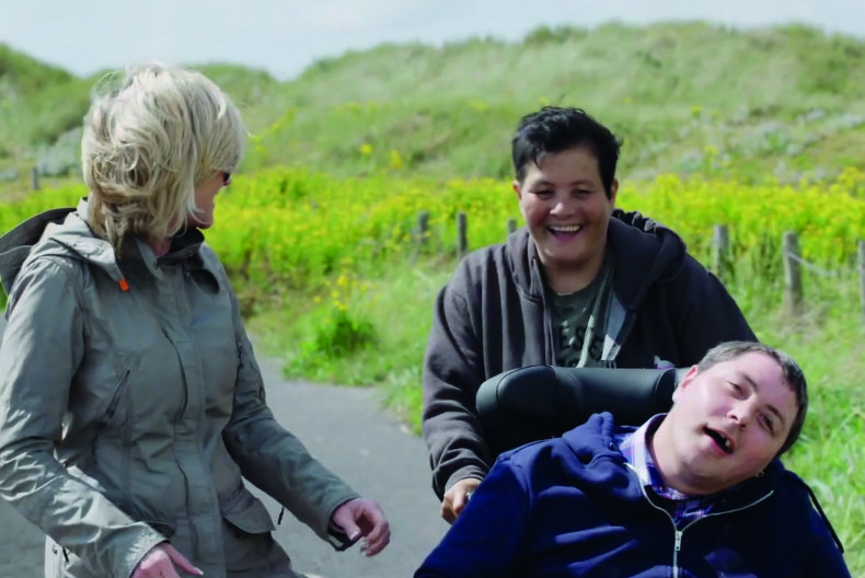 Revitalise guest Shaun being pushed in a wheelchair by his mother and carer Hilary on a sunny day