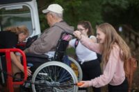 Young female volunteer helping man in wheelchair into a van