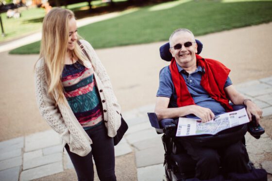 Young female volunteer walking with an older disabled man in a wheelchair