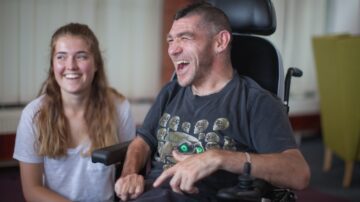 Man in wheelchair and a young female volunteer laughing together at Revitalise Sandpipers