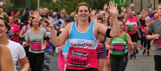 Woman running the Great North Run for Revitalise wearing teal and pink Revitalise running jersey