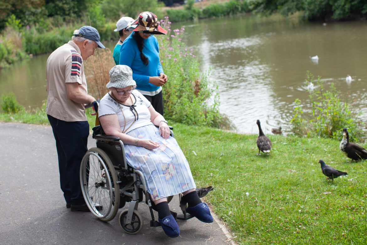 Woman in wheelchair with two young people and an older man feeding ducks in Southport