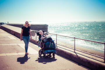 Disabled man in wheelchair walking down Southampton boardwalk with a young woman