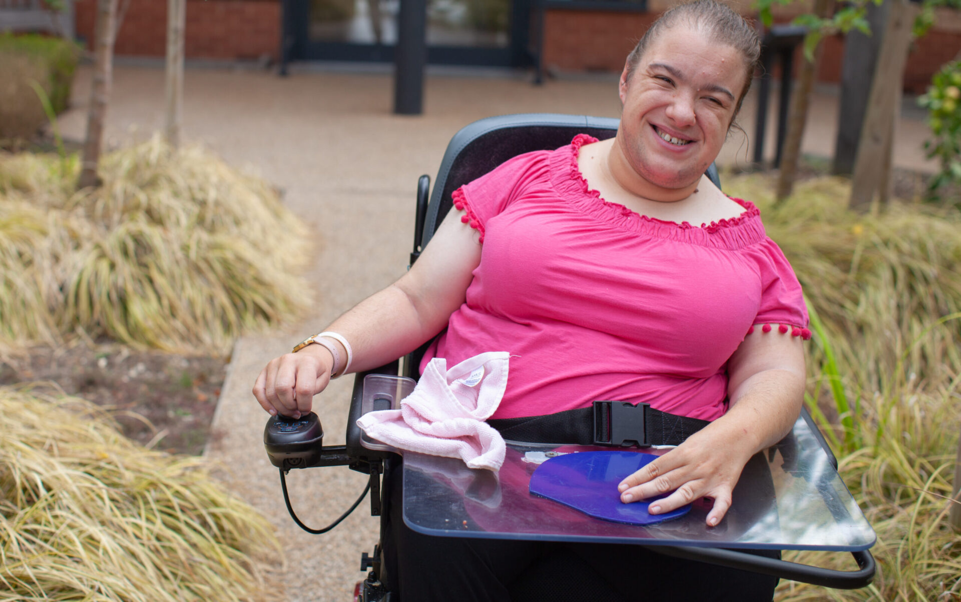 Disabled woman in an electric wheelchair smiling for the camera while enjoying time in Revitalise Jubilee Lodge's courtyard.