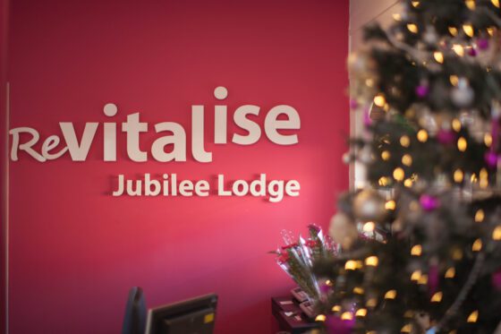 Revitalise Jubilee Lodge lobby decorated for Christmas with a lit up tree in the foreground and the name of the centre on a pink wall in the background