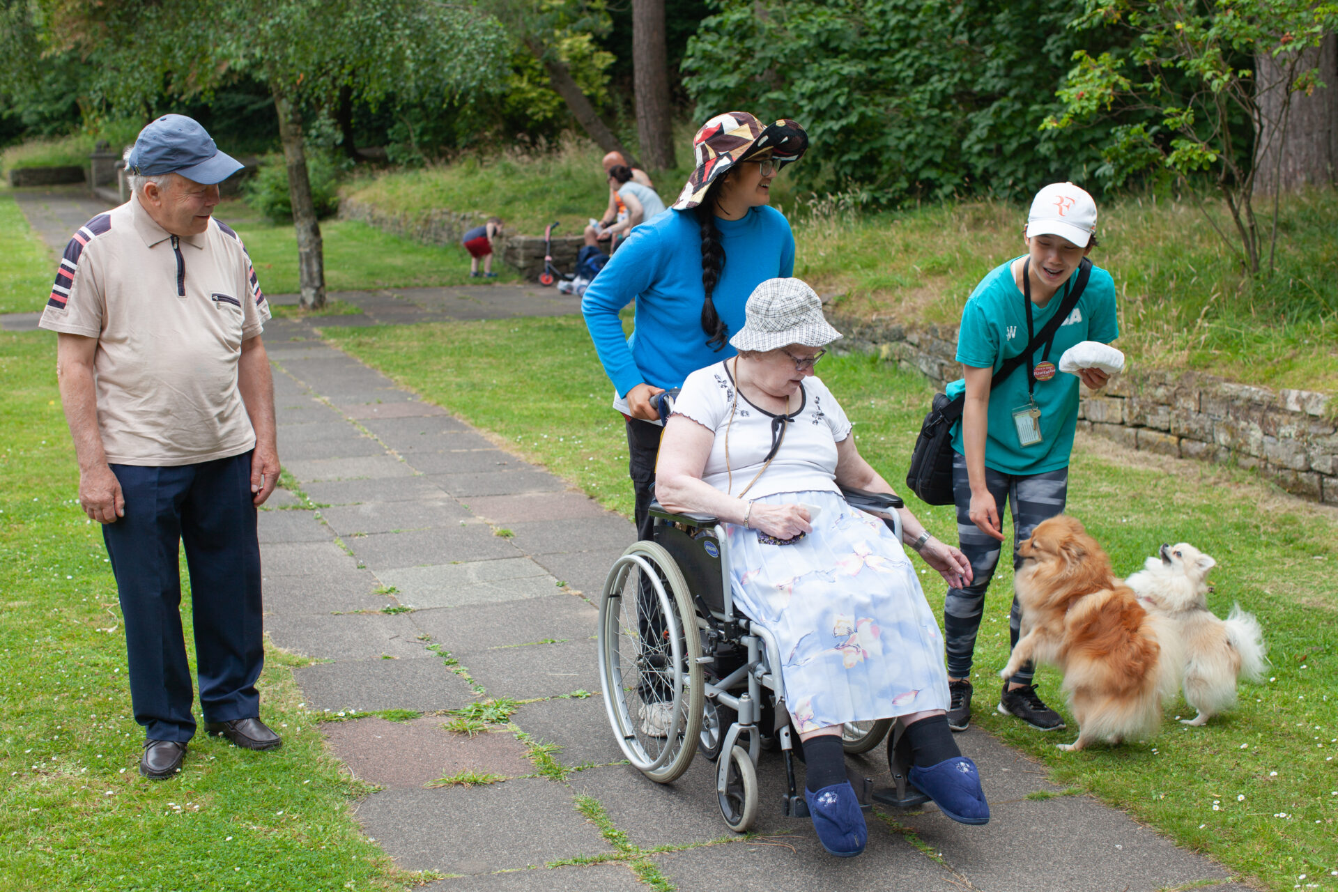 Woman in wheelchair petting two pomeranian dogs while on a walk with an older man and two young women