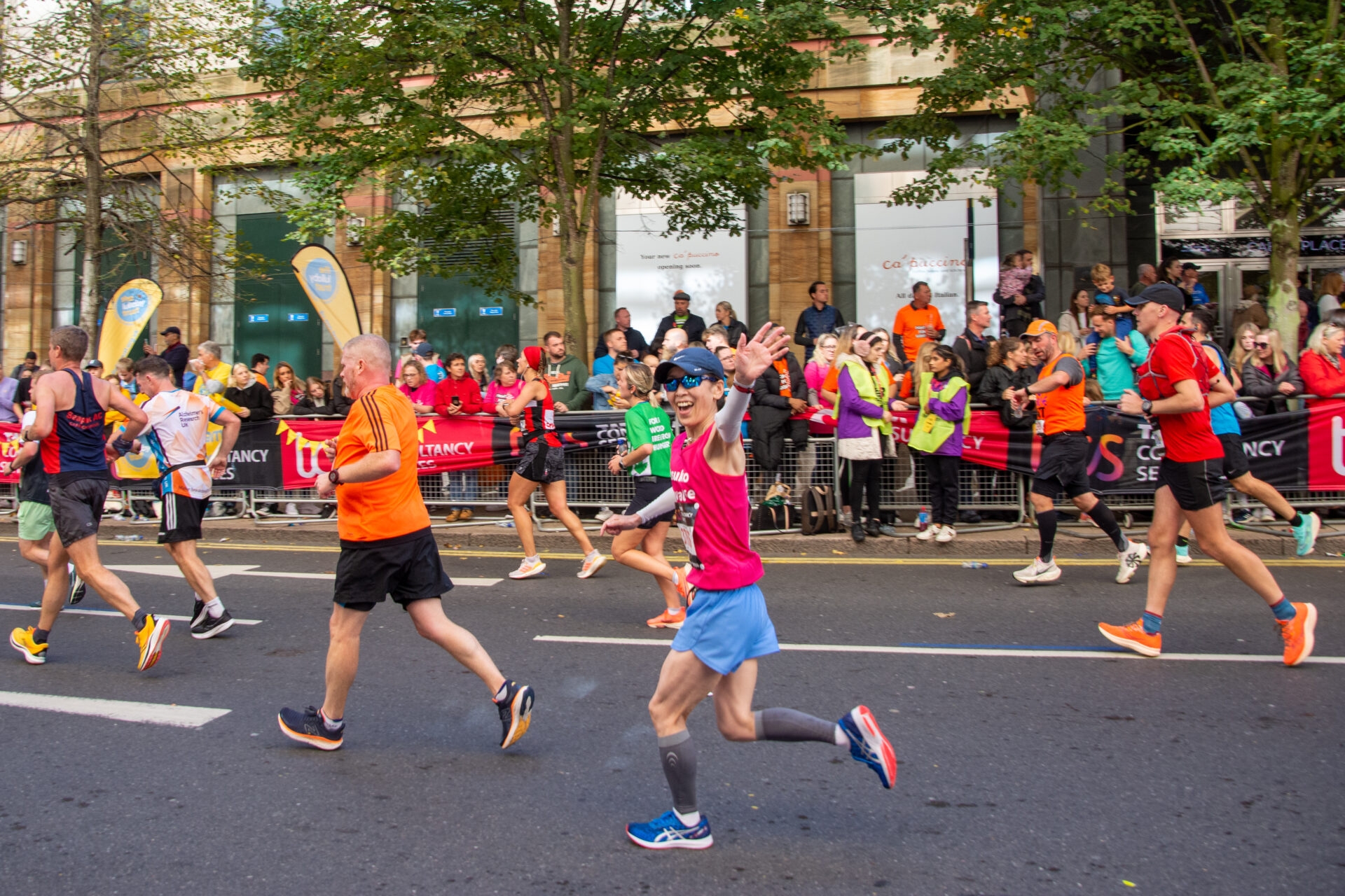 Female runner waving at camera while running the London Marathon through Canary Wharf