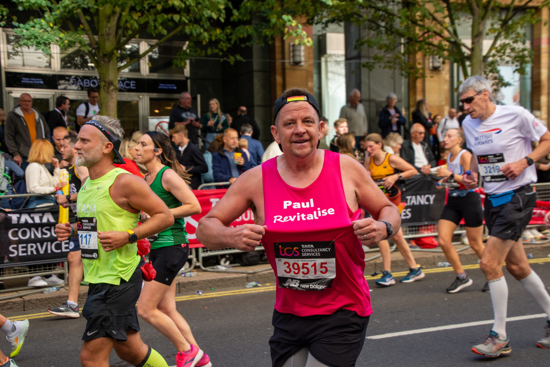 Man running the London Marathon holding his pink jersey to display the Revitalise logo