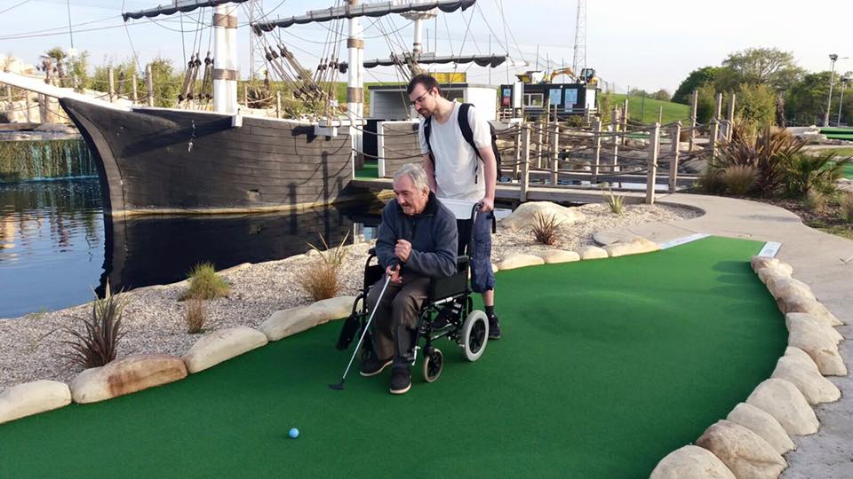 Man in wheelchair playing mini golf with assistance from a young male volunteer