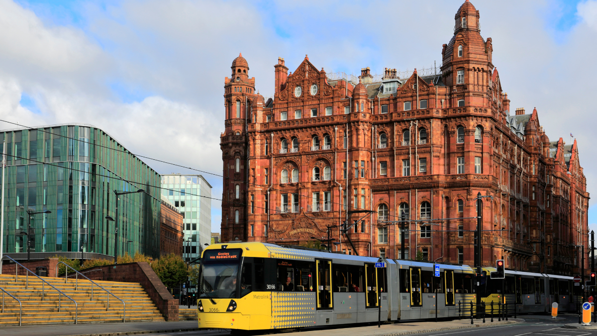 A long shot view of the Manchester city on a bright day. The famous Midland Hotel can be seen in the background with the iconic yellow tram in the front.