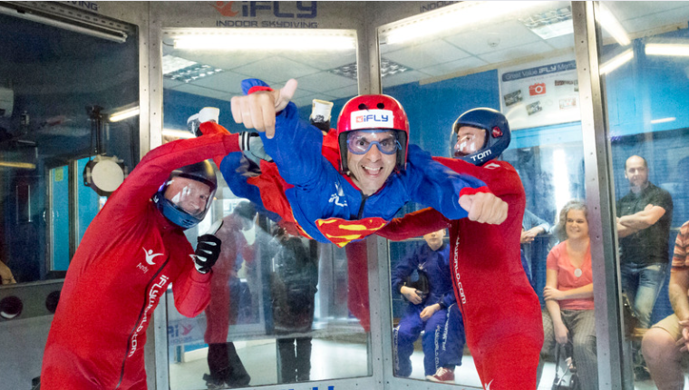 A guest at Revitalise is enjoying the thrill of indoor skydiving at iFLY London. The guest is smiling and giving a thumbs up to the camera.