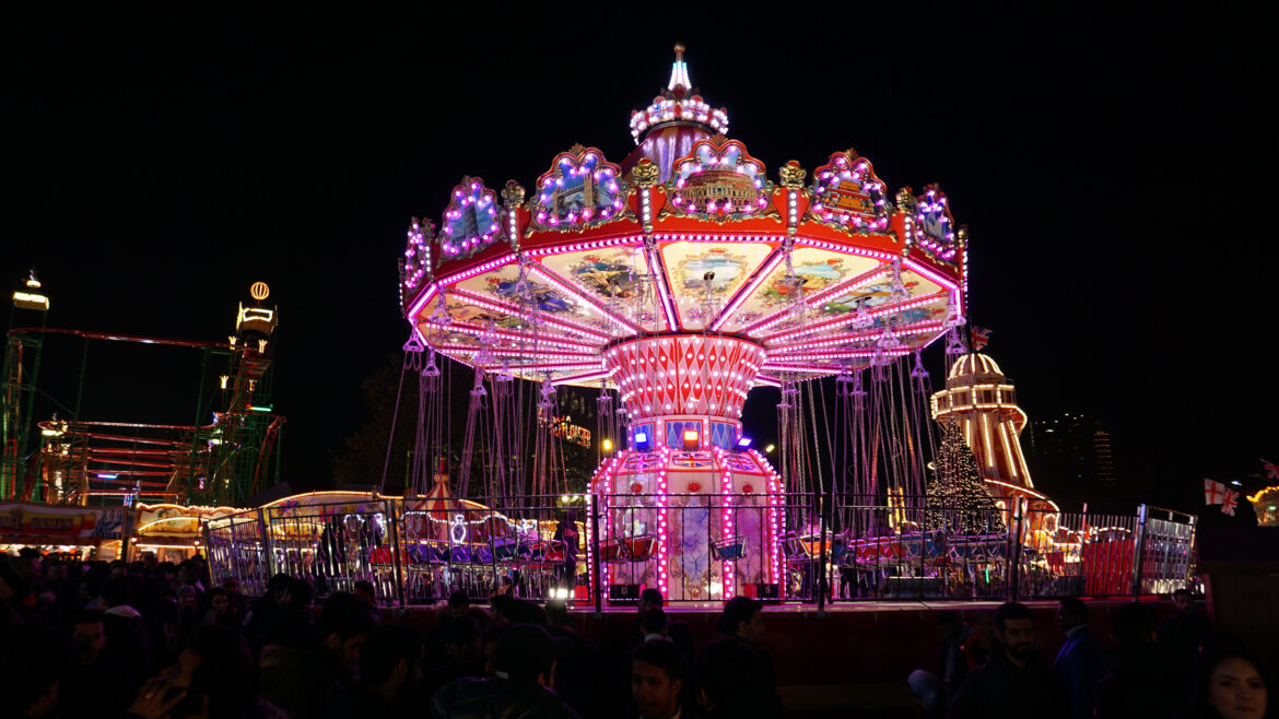 Night photo of festive carousel lit up in pink and purple lights at Winter Wonderland in Hyde Park, London