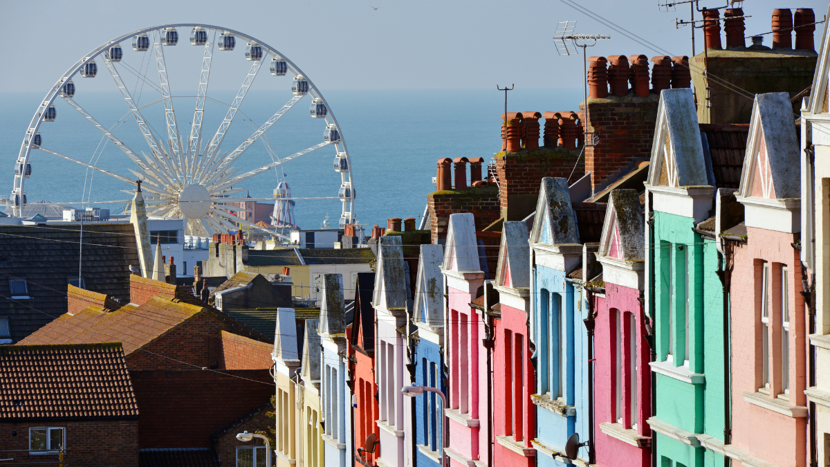 Image shows a popular street on on the Albion Hill in Brighton. The street's pastel-coloured beautiful houses are neatly lined on one side of the image. The other side of the image shows the Brighton Ferris wheel in the background.