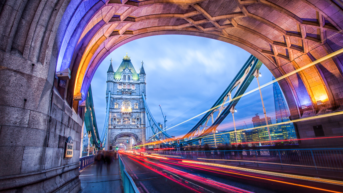 Image of London's iconic Tower Bridge. The image is shot through a tunnel and is edited to add yellow and red streaks running under the tower on the bridge.