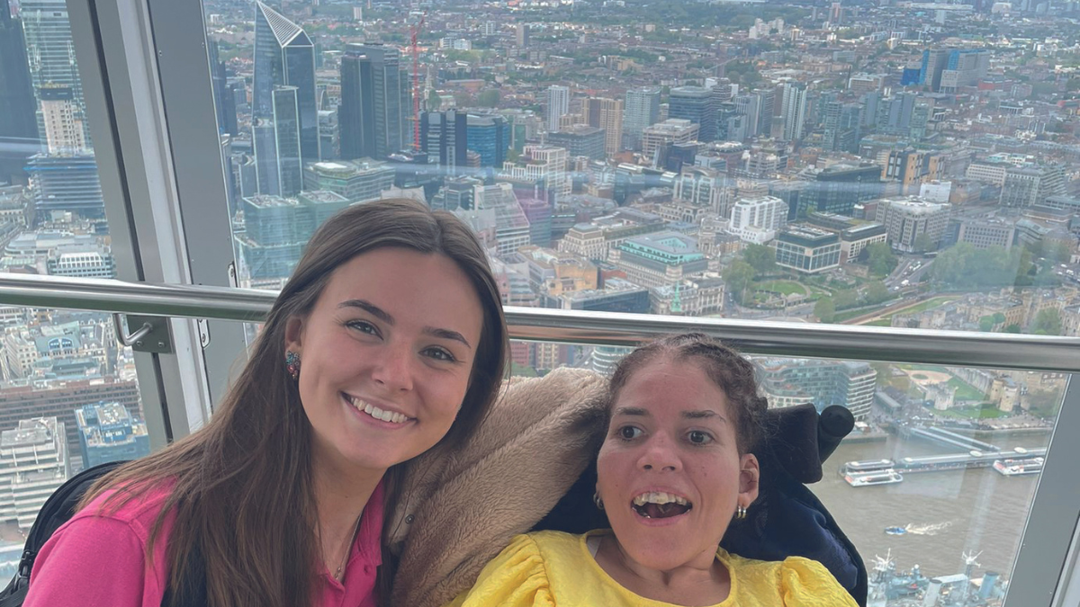 A guest and a care member from Revitalise Jubilee Lodge smiling at the camera on their excursion to Sky Garden. The breathtaking view of London's skyline is seen in the background.