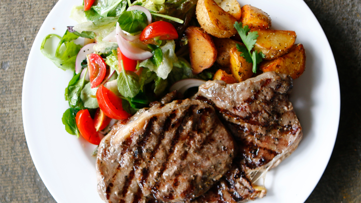 Image of a plate of steak and roasted potatoes topped with a salad of tomatoes and lettuce.
