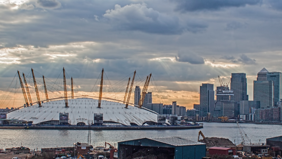 Image shows along shot of the Greenwich skyline in London with river Thames and O2 arena in the foreground. The sky is filled with grey stratus clouds.