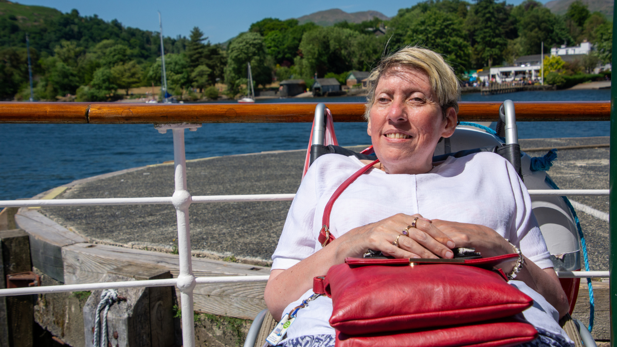 Image of a guest from Revitalise Sandpipers sitting on a boat on a sunny day and enjoying a cruise on Lake Windermere.