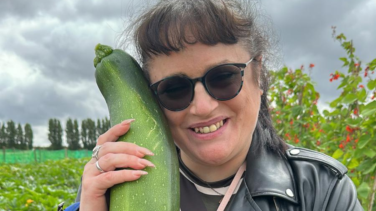 A guest from Revitalise Jubilee Lodge out on an accessible excursion to a pick your own farm. The guest is holding a courgette and smiling at the camera.