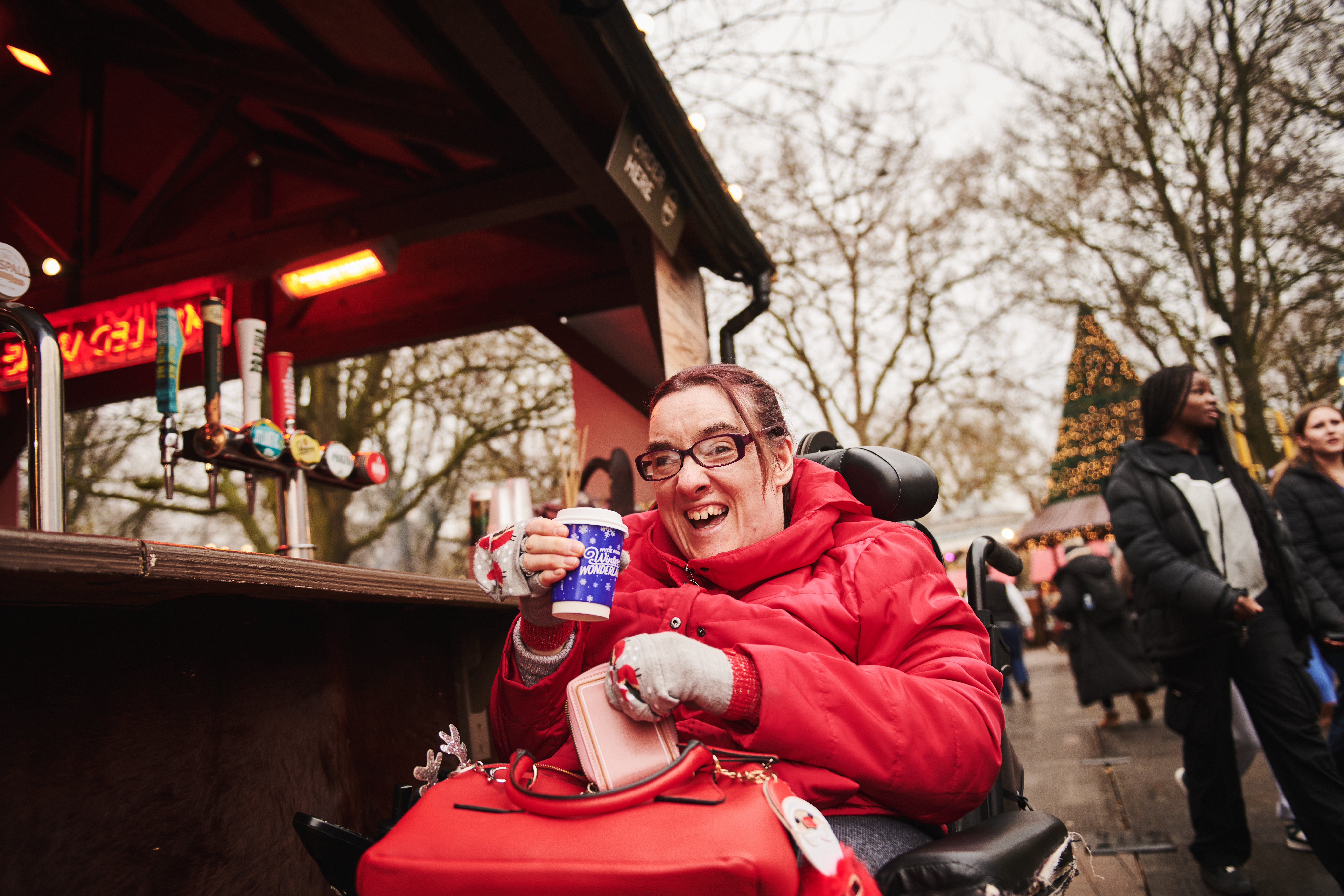 A guest from Revitalise Jubilee Lodge is drinking a cup of hot mulled wine while enjoying their day at the Hyde Park Winter Wonderland