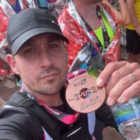 A runner from Team Revitalise holding the London Marathon 2024 medal.