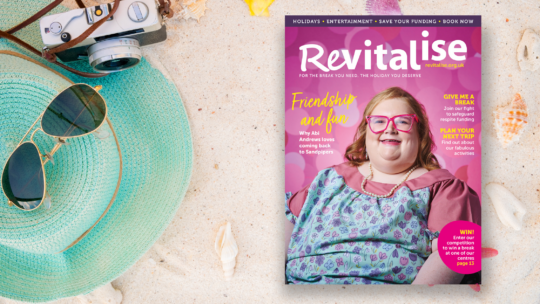 Close up image of sand on a beach along with a sun hat and a camera, suggesting holidays. An image of the front cover of Revitalise spring 2024 magazine is overlayed.