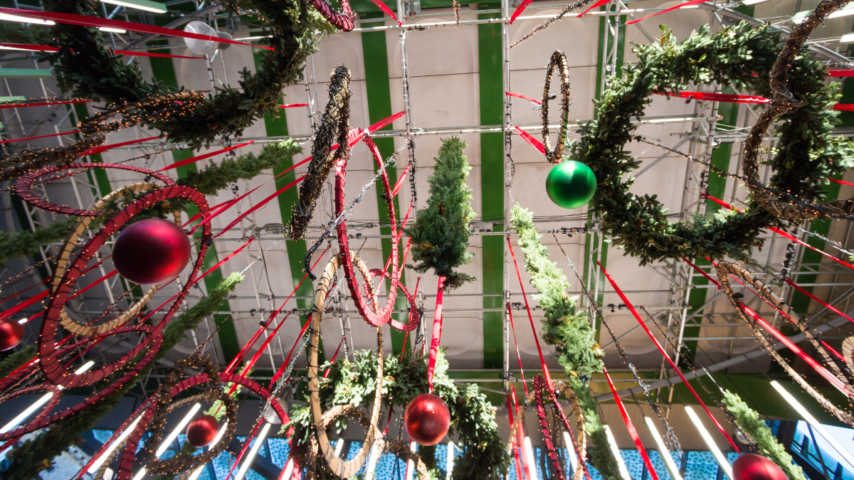 The image showcase red and green-coloured huge Christmas wreaths and baubbles decorated from the ceiling at a street market. The wreaths are decorated with tinsels and fairy lights.